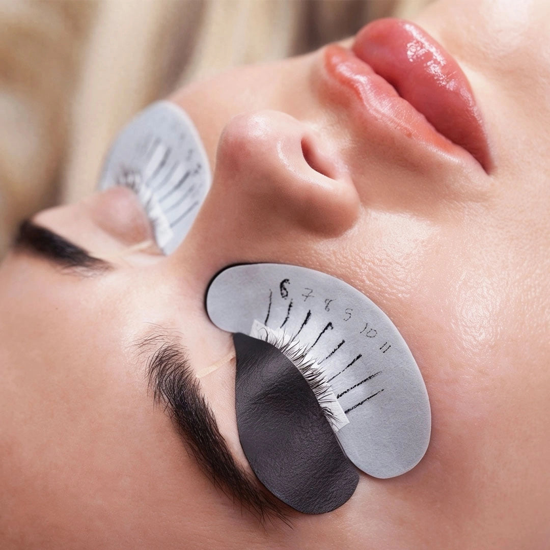 Gros plan d’une cliente portant des patchs noirs bio-gel sur les paupières supérieures et des patchs blancs de mapping sous les yeux pendant une pose d’extensions de cils.