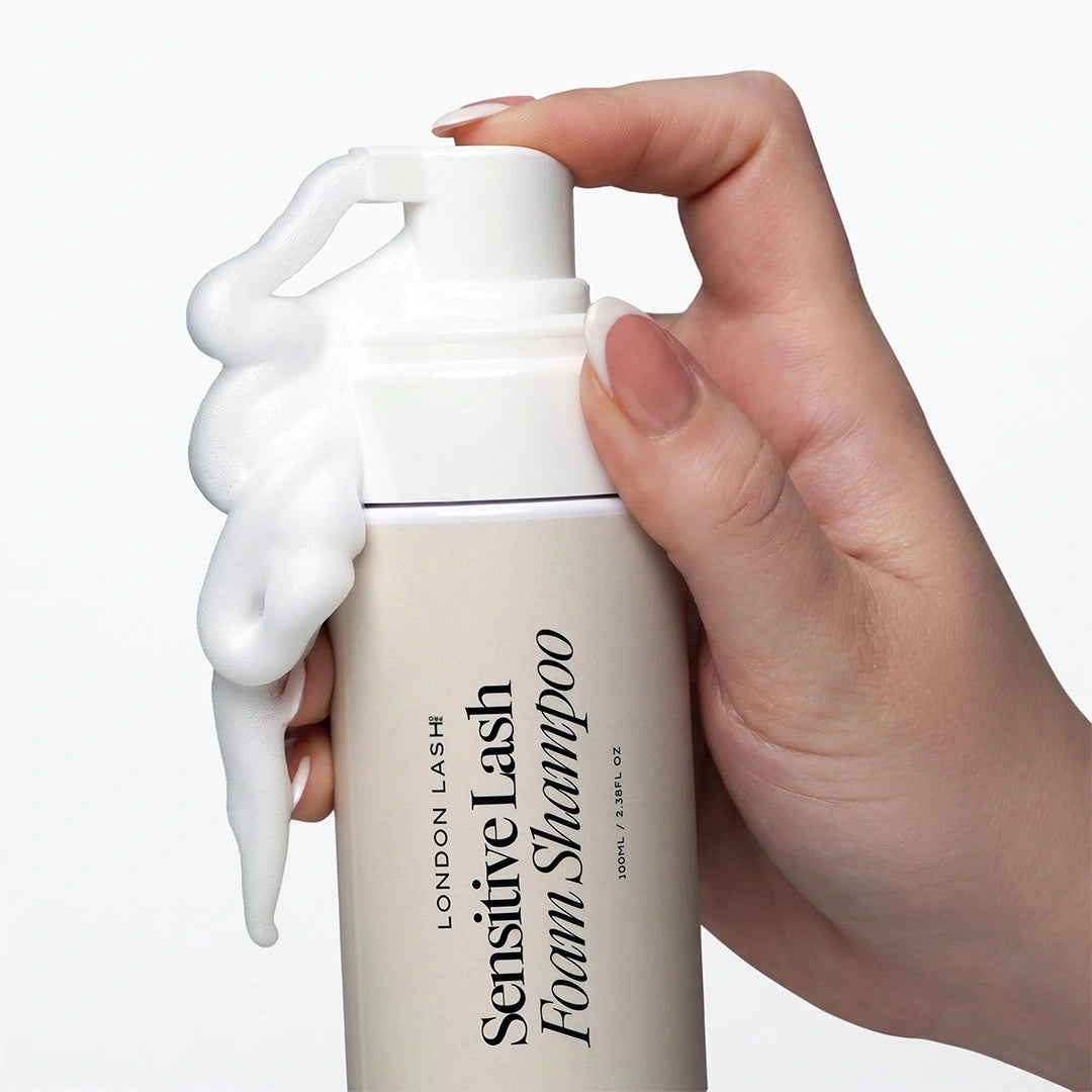Gros plan d'une main appuyant sur la pompe du Sensitive Lash Foam Shampoo London Lash pour distribuer une mousse nettoyante riche.