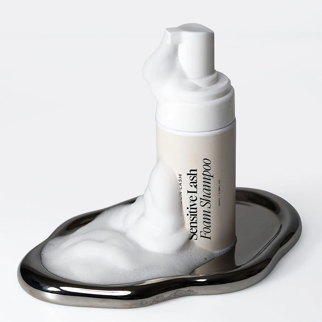 Sensitive Lash Foam Shampoo London Lash présenté sur un plateau argenté réfléchissant, entouré d'une mousse nettoyante abondante.